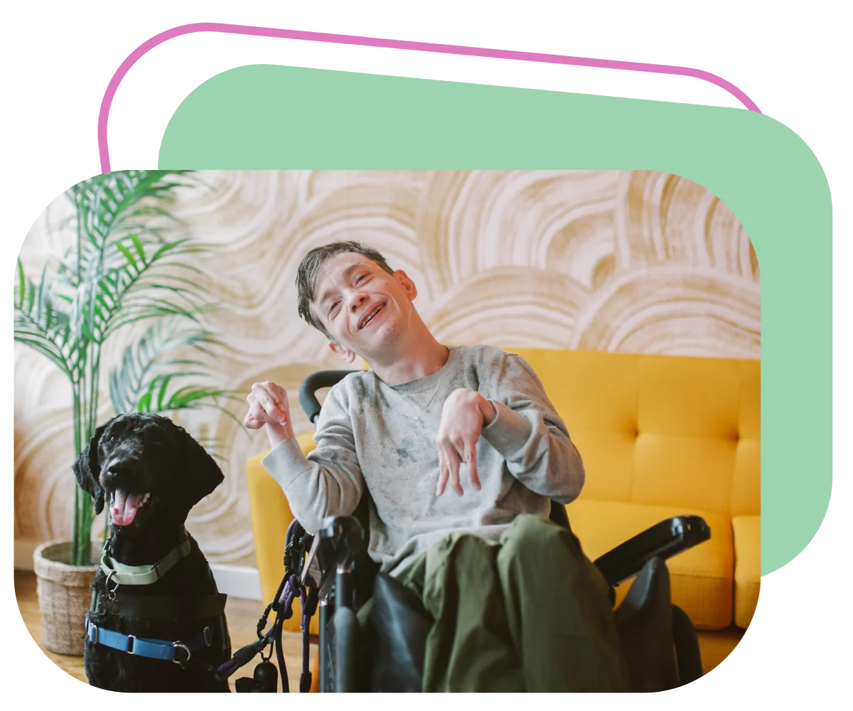 A disabled young man is smiling while sitting in his wheelchair. His support dog is sitting next to him