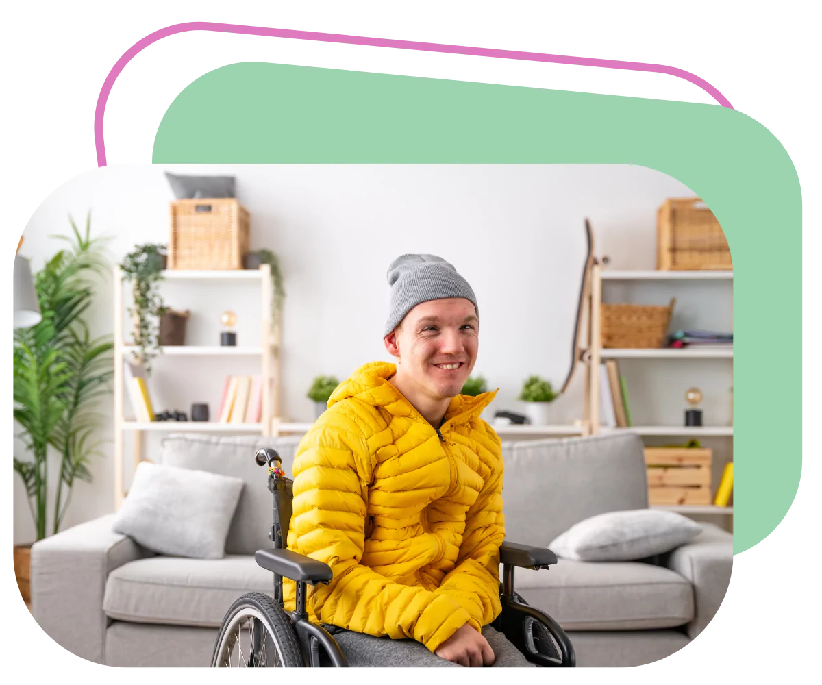 A young disabled man is smiling at the camera while sitting in his wheelchair. He's indoors keeping warm and the room looks very comfortable